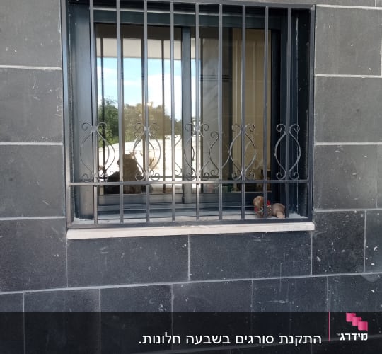 חלון עם סורגים מתכתיים על קיר אפור